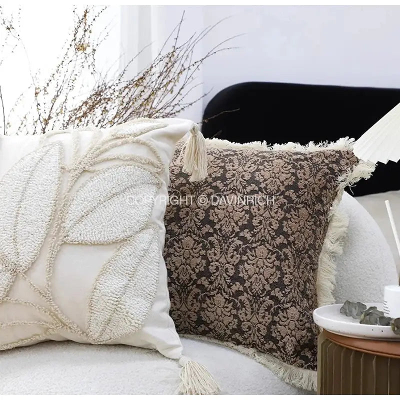 Cream-colored geometry tufted cushion cover with textured leaf embroidery and tassels paired with brown damask pillow decorbites boho leaf