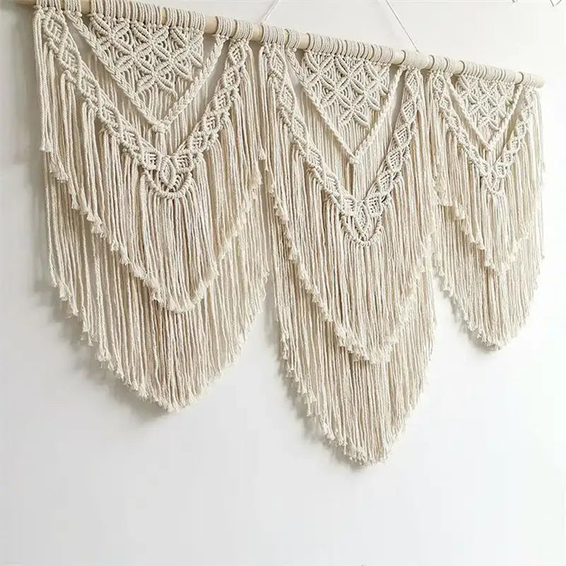 Cream-colored macrame wall hanging tapestry with intricate geometric patterns and long flowing fringe for boho decor