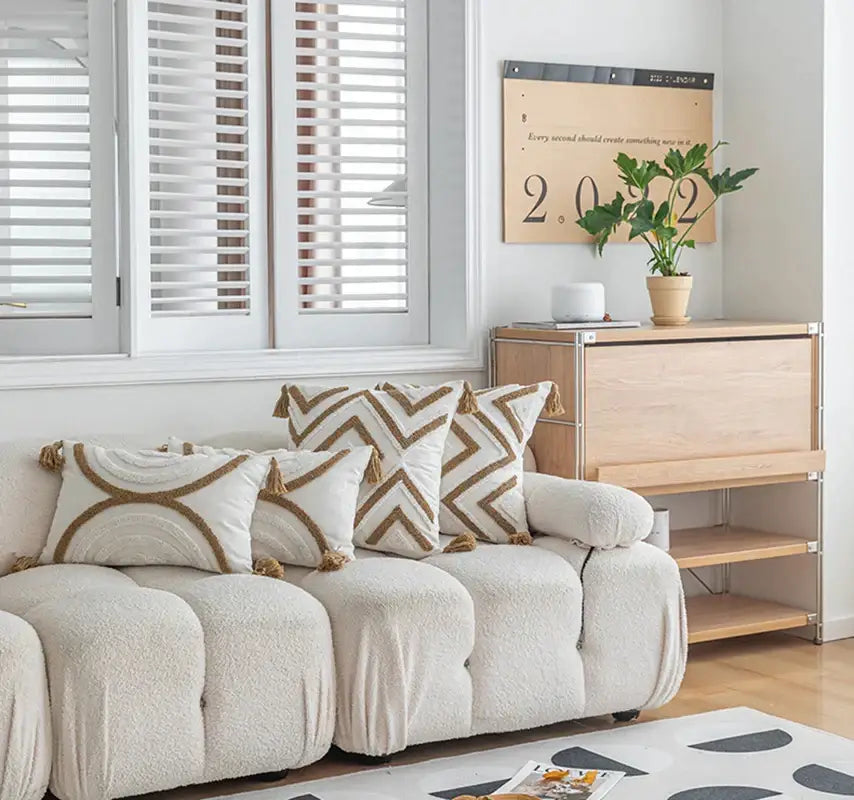 Cream-colored plush tufted sofa with beige and cream boho cushion covers featuring geometric tufted fringe pillows