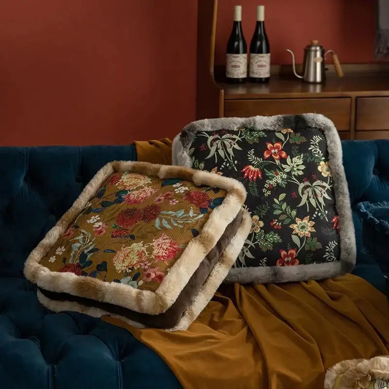 Two boho dark floral square seat cushions with gray faux fur trim resting on a velvet dining room sofa