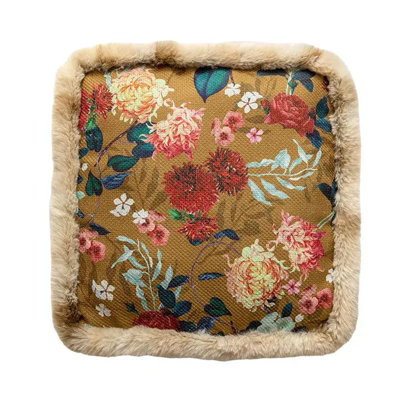 Square-shaped cushion with a rich mustard-yellow fabric featuring an intricate floral pattern in shades of pink, red, and teal, bordered by soft beige faux fur.
