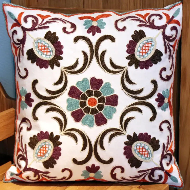 White cushion with intricate embroidered ethnic flower elephant floral patterns in burgundy teal orange and brown decorbites pillowcase