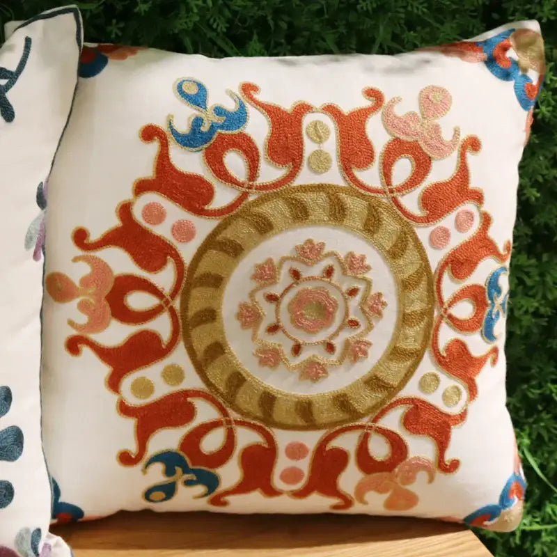A square white cushion with intricate orange gold and blue embroidery featured in decorbites ethnic flower pillowcase