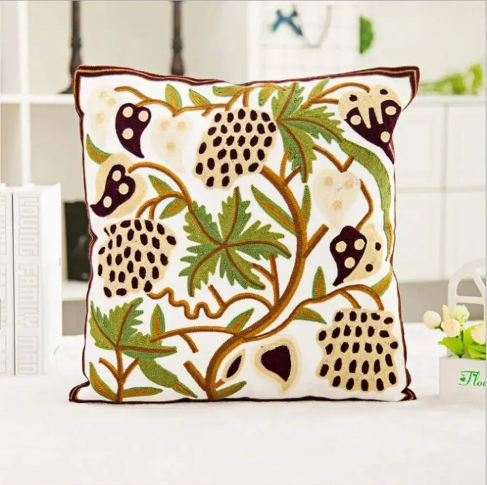 White cushion with intricate embroidered boho farmhouse floral design featuring green leaves and dark purple berries on cream pillow cover decorbites