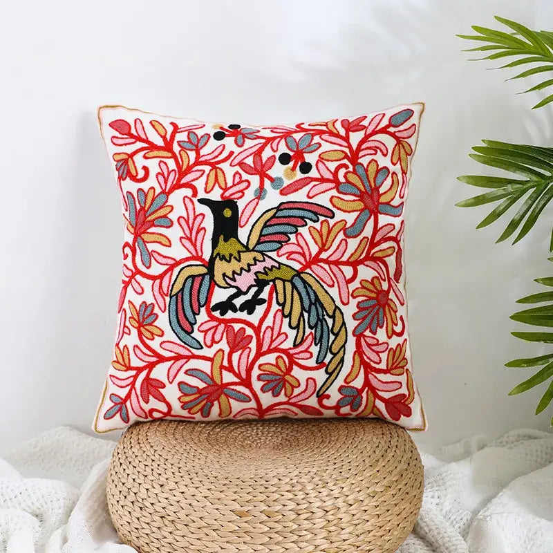 Vibrant square cream pillow covers with intricate red and blue embroidered floral patterns and a central colorful bird decorbites boho farmhouse floral design
