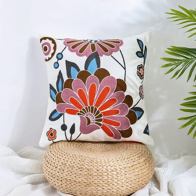 White pillow cover with vibrant boho farmhouse floral embroidery in pink orange brown petals and blue leaves by decorbites