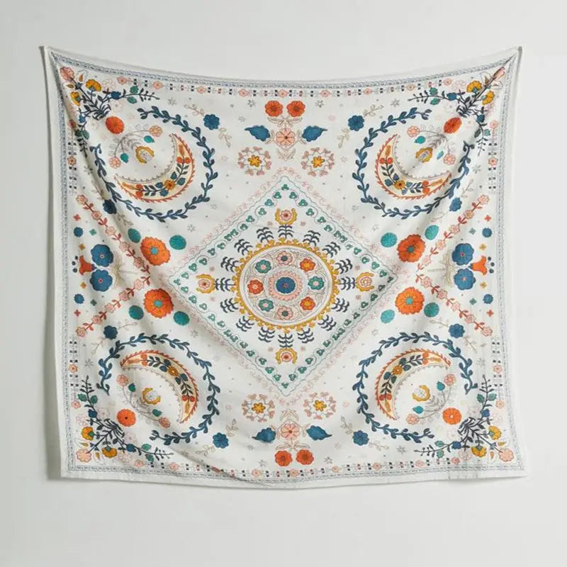 A square white embroidered wall tapestry featuring vibrant orange and blue flowers crescent moons and geometric designs for boho floral celestial decorbites decor