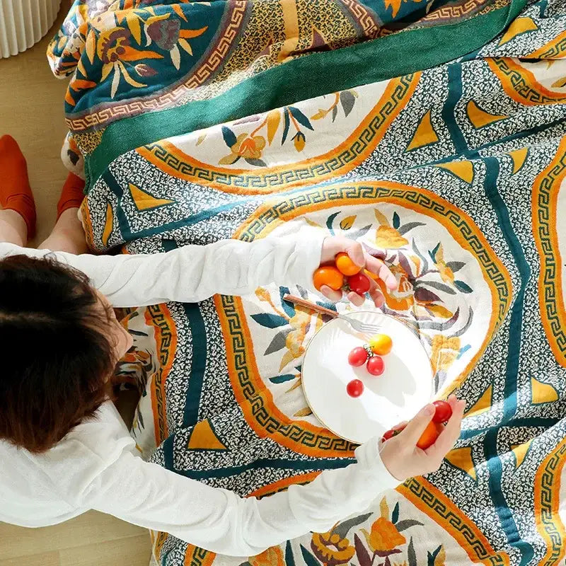 A person seated on a patterned boho floral cotton gauze leisure blanket in teal orange and yellow decorbites cotton gauze