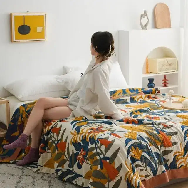 A vibrant boho floral cotton gauze leisure blanket with bold orange blue and green botanical patterns on cream background