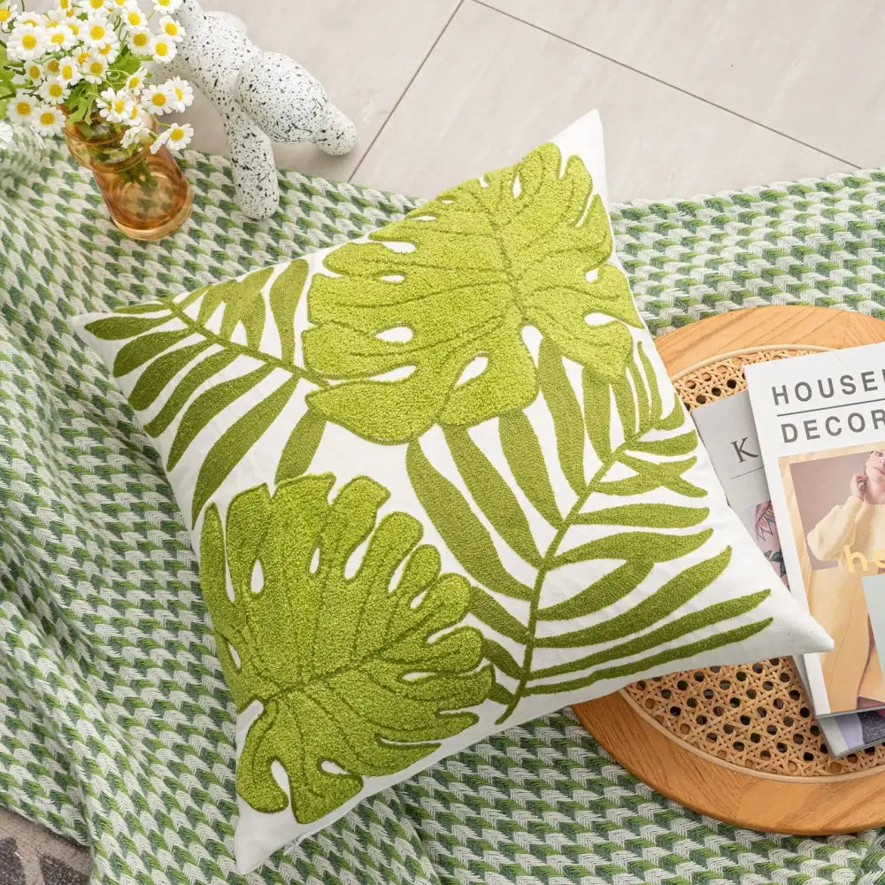 A square white cushion featuring vibrant lime green embroidered tropical leaf patterns.