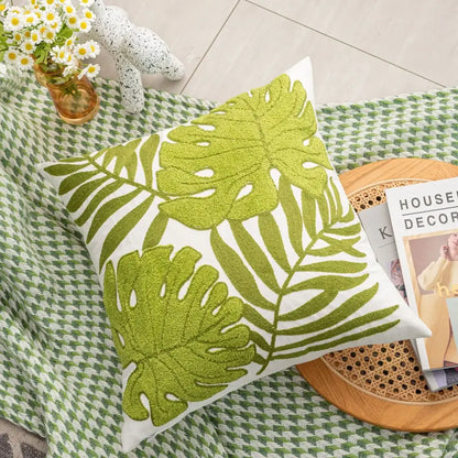A square white cushion featuring vibrant lime green embroidered tropical leaf patterns.