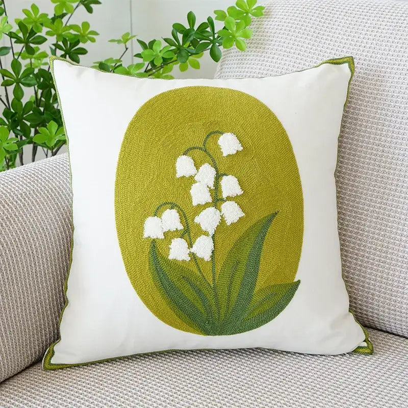 White cushion cover with boho floral embroidered lily-of-the-valley on olive green oval background by decorbites