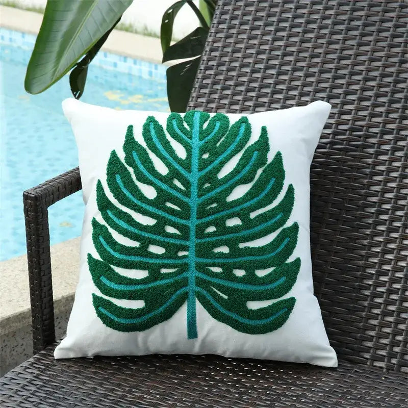White cushion featuring a prominent embroidered monstera leaf in shades of green and teal.