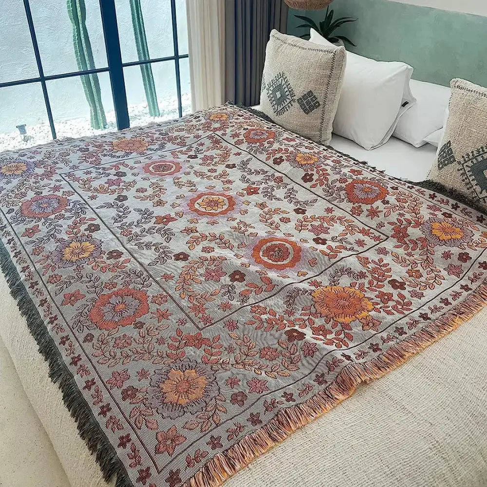 A cozy light gray boho floral sofa throw blanket with intricate warm orange patterns and fringed edges for decorbites boho floral decor