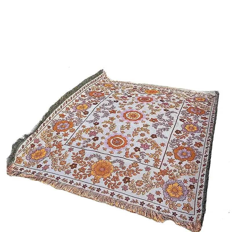 A soft, light gray throw blanket featuring a vibrant floral pattern in shades of orange, purple, and brown with fringed edges.
