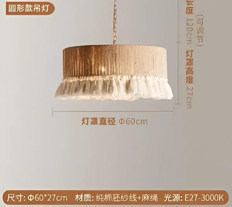 A round pendant light with a gold-toned, fringed fabric shade and white tassels hanging from the bottom.