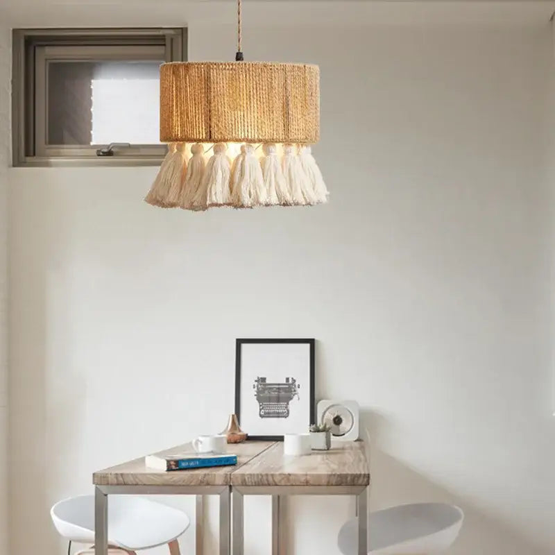 A warm-toned, cylindrical pendant lamp with a woven natural fiber shade and soft white tassels hanging below.