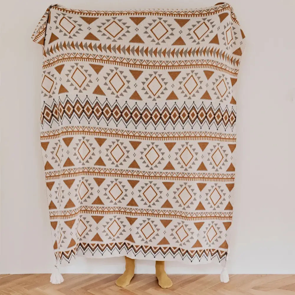 A cozy cream-colored decorbites boho geometric pattern throw blanket with warm brown and gray tones and tassels at corners