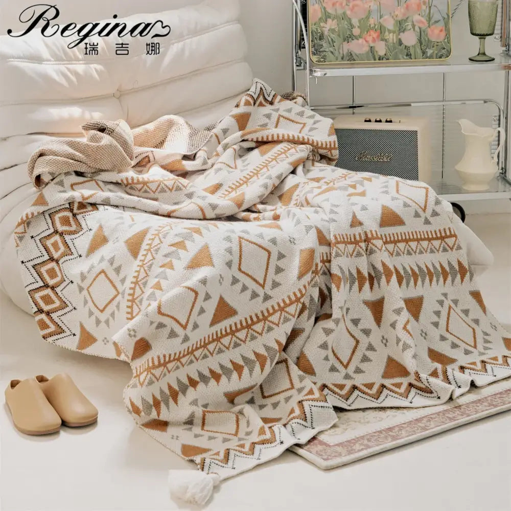 A cozy cream-colored throw blanket with boho geometric pattern in brown and gray tones featuring tassels
