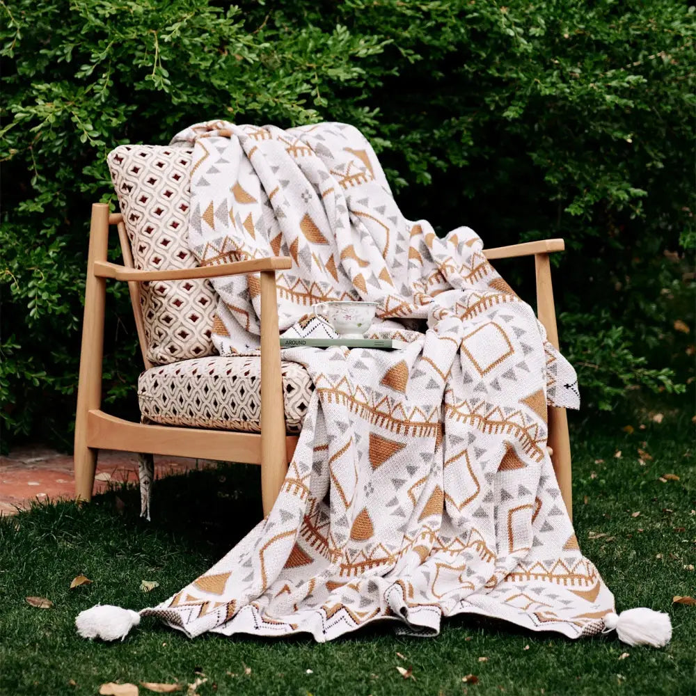 A cozy cream-colored throw blanket with a boho geometric pattern in tan and gray featuring tassels by decorbites