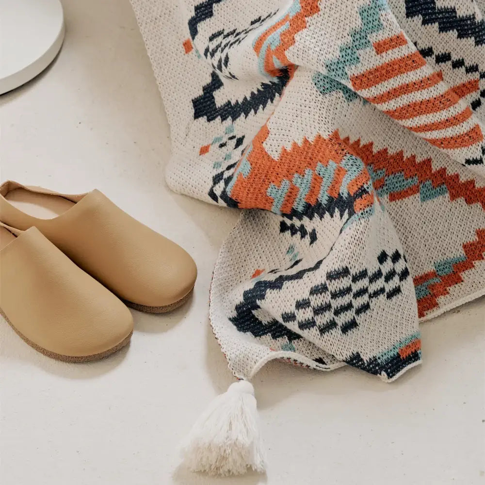 A cozy cream-colored knitted decorbites boho geometric summer blanket with orange teal navy patterns and white tassel corner