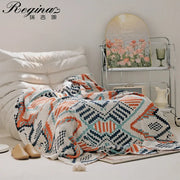 A cozy, hand-knitted throw blanket with a geometric pattern in orange, teal, and navy on a cream base.