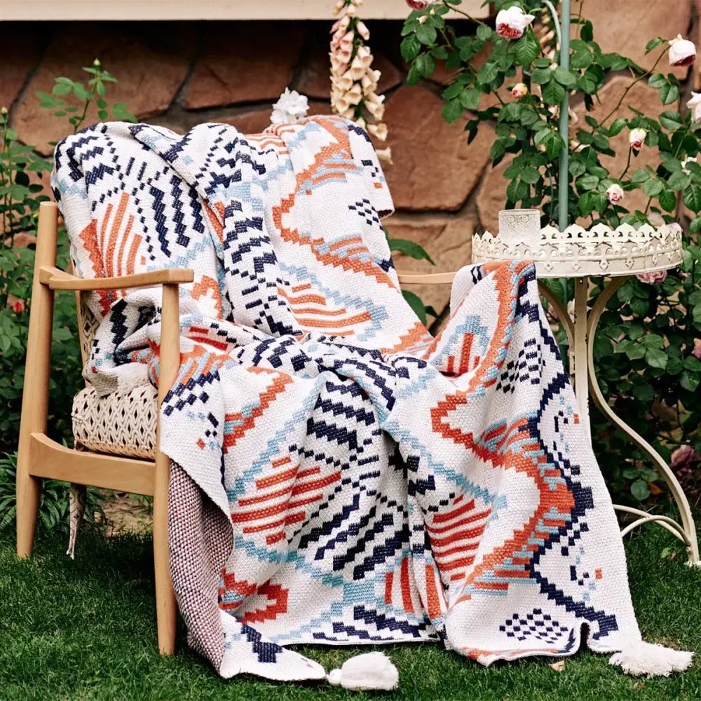 A cozy, knitted throw blanket with a geometric pattern in white, navy blue, orange, and light blue hues.
