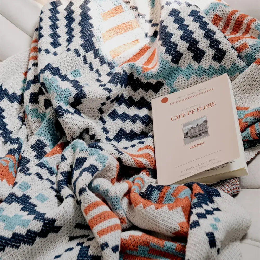 A cozy knitted boho geometric summer blanket with navy blue teal and orange on white decorbites bedroom throw