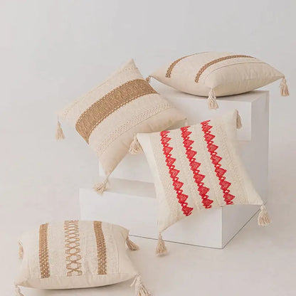 Beige and red embroidered throw pillows with woven stripes, tassels, and textured fabric.