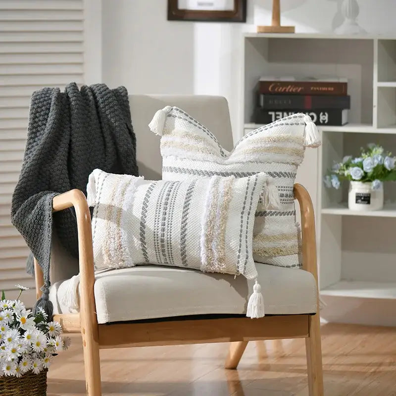 Two off-white and gray boho geometric tufted cushion covers with tassels on light wood armchair decorbites pillow