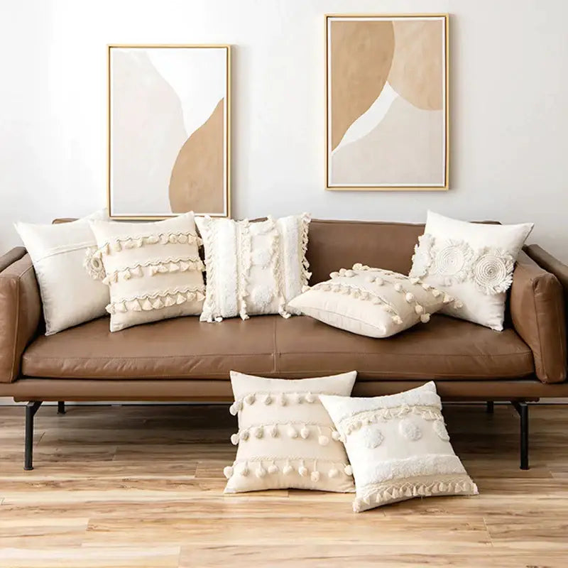 Cream-colored boho ivory cushion cover with textured tassels and pom-poms on brown leather sofa decorbites ivory cushion