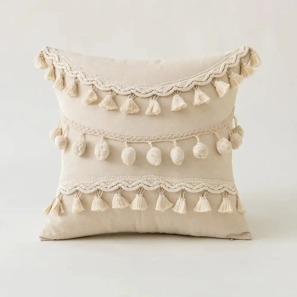 Beige boho ivory cushion cover with three horizontal rows of decorative tassels and pom-poms for living room sofa decor