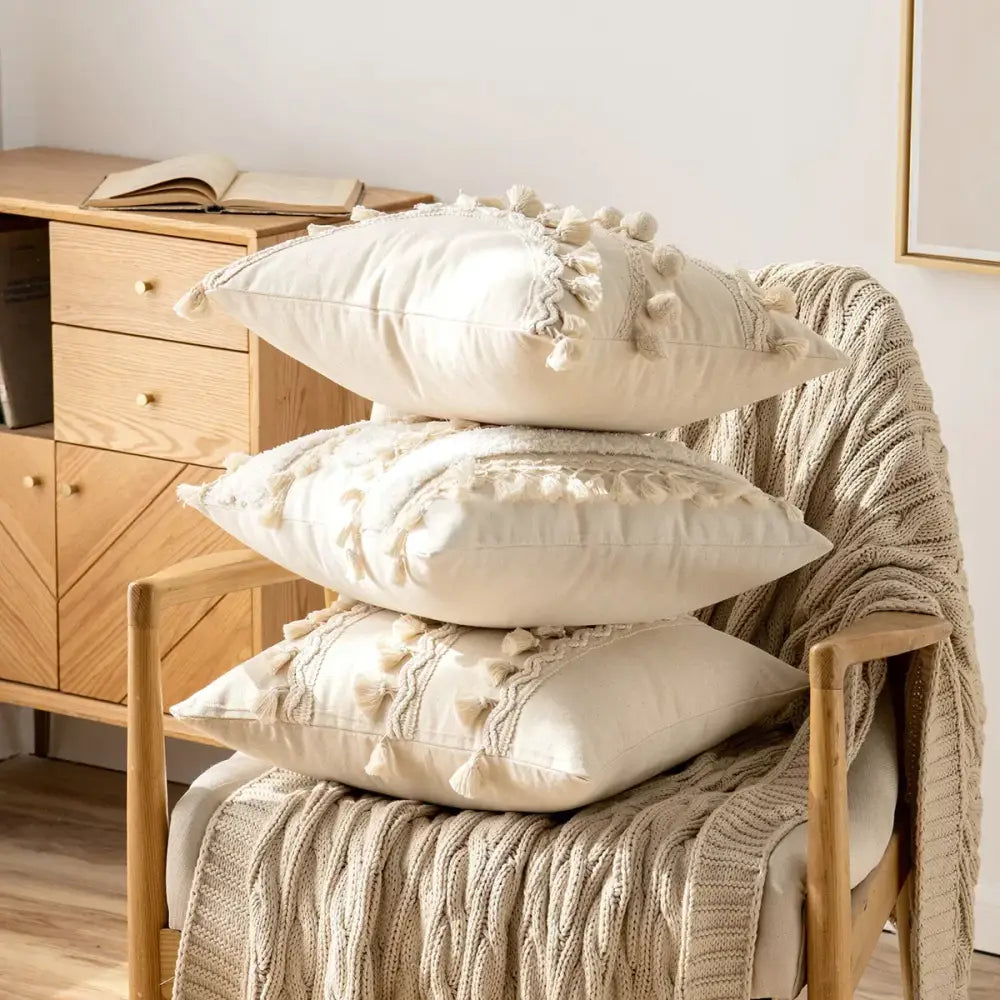 Stack of three cream-colored boho ivory cushion covers with pompoms lace and textured tassel trim for living room decor