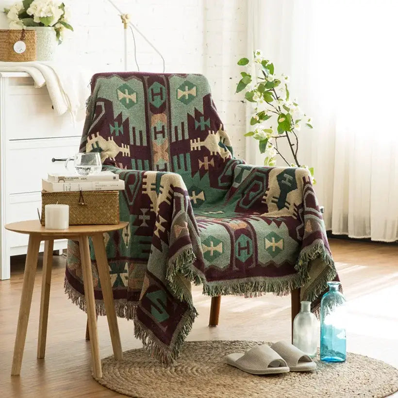 A cozy decorbites boho jacquard knit throw blanket in green maroon and beige geometric pattern draped on an armchair