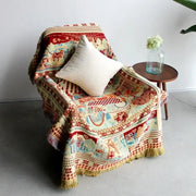 A cozy boho jacquard knit throw blanket in rich reds and creams with animal and architectural designs draped over a chair