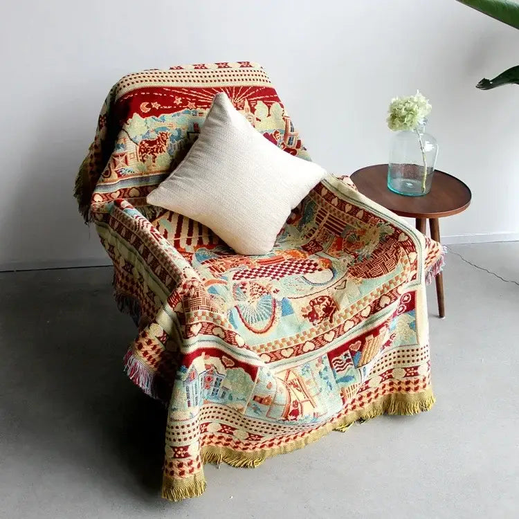 A cozy boho jacquard knit throw blanket in rich reds and creams with animal and architectural designs draped over a chair