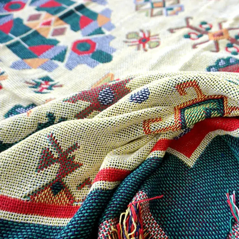 A boho jacquard knitted throw blanket with vibrant geometric patterns in red green blue and orange on a cream base