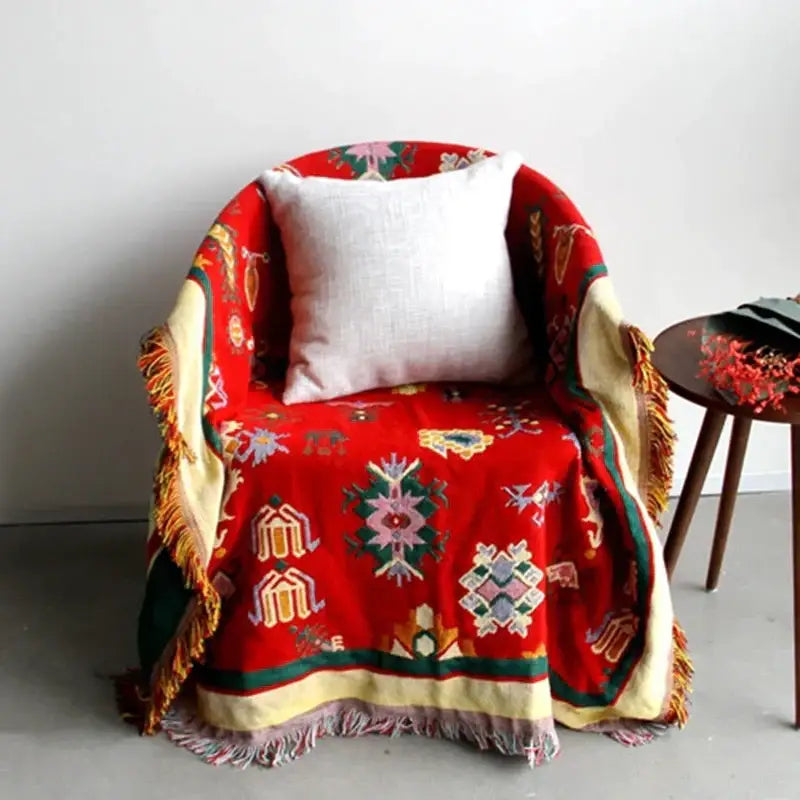 A vibrant red decorbites boho jacquard knitted throw blanket with pastel embroidery and cream fringe for living room decor