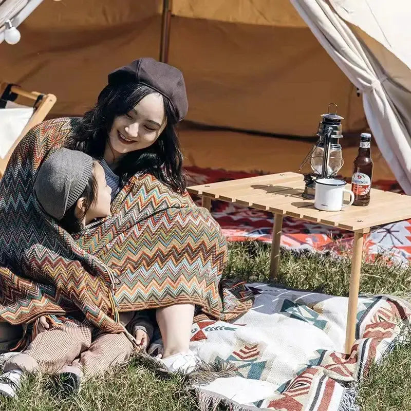 A cozy boho knitted striped blanket with tassels in warm earthy tones draped over a woman and child