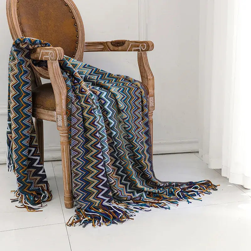 A vibrant multicolored boho knitted striped blanket with tassels draped over a wooden chair for living room decor
