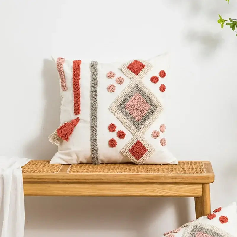 A cream-colored decorbites boho loop tufted pillow cover with embroidered geometric patterns and tassel accents