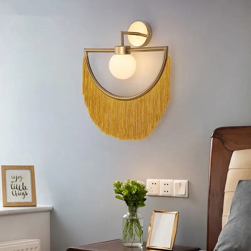 Gold-toned wall sconce with frosted glass ball pendant and cascading mustard-yellow fringe for boho bedroom décor