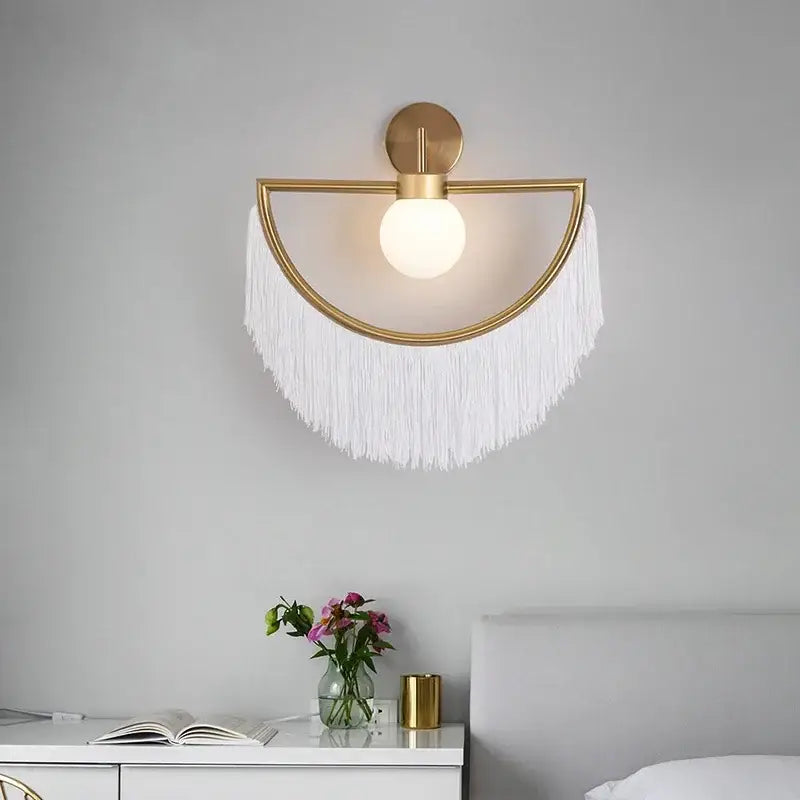 Gold-toned semi-circular wall sconce with frosted glass globe and white fringe for boho glass ball pendant light
