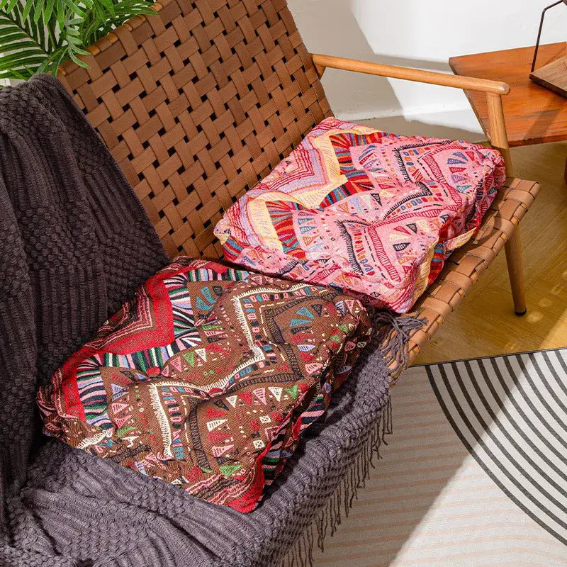 Two colorful boho square floor pillows with geometric tribal patterns on a woven wicker chair for living room seating