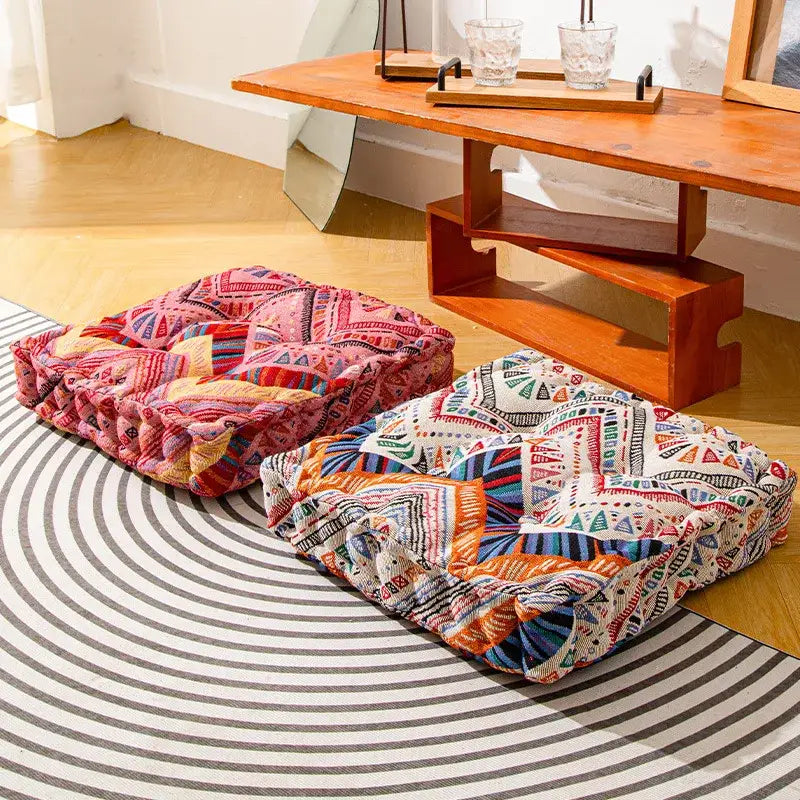 Two colorful boho square floor pillows with vibrant geometric patterns sit on a striped rug for living room seating