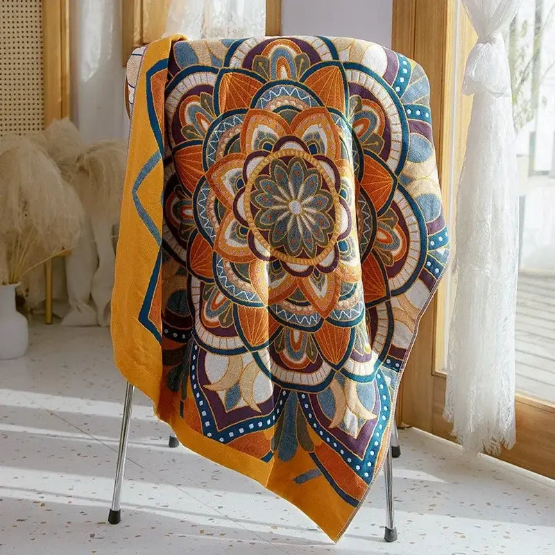 A vibrant orange and blue mandala-patterned boho patchwork cotton gauze bath towel draped over a metal chair