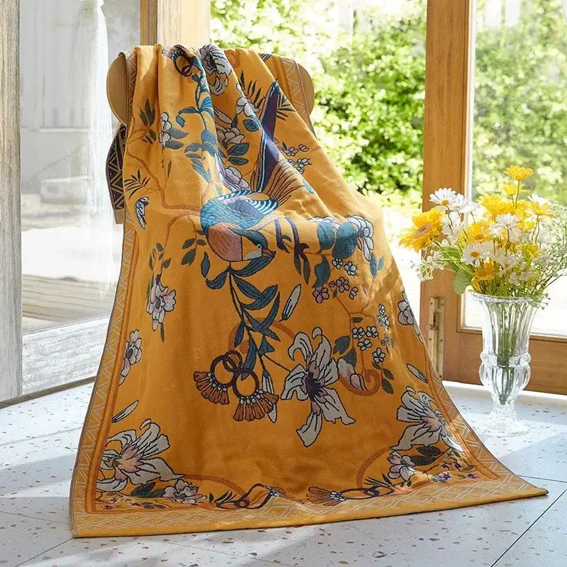 A vibrant yellow cotton gauze bath towel with intricate blue floral and bird patterns from decorbites