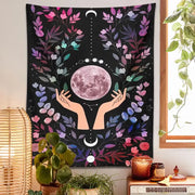 A vibrant black boho pink botanical moon tapestry with a central pinkish-purple moon and colorful floral motifs