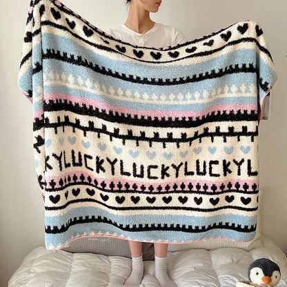 A cozy boho printed blanket with light blue pink cream stripes black heart motifs and lucky lettering perfect for bedrooms