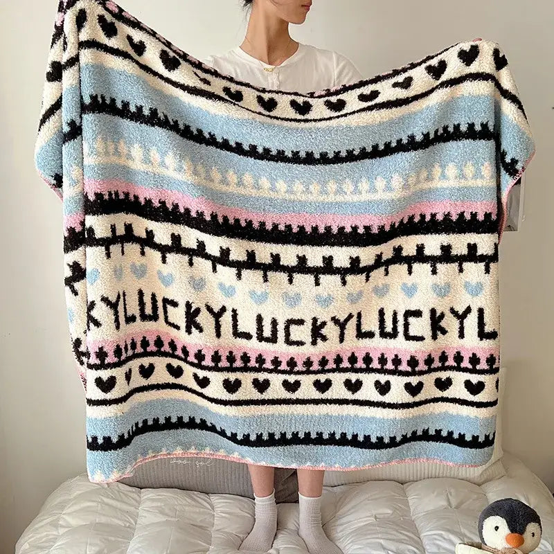 A cozy boho printed blanket with light blue pink cream stripes black heart motifs and lucky lettering perfect for bedrooms